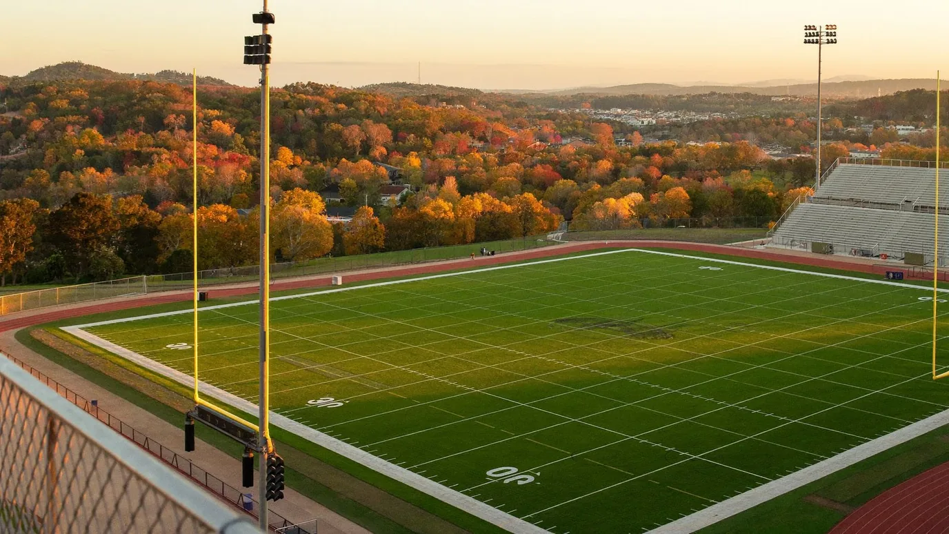 Stadium fundraiser example — a high school football stadium and running track at golden hour, autumn hills beyond
